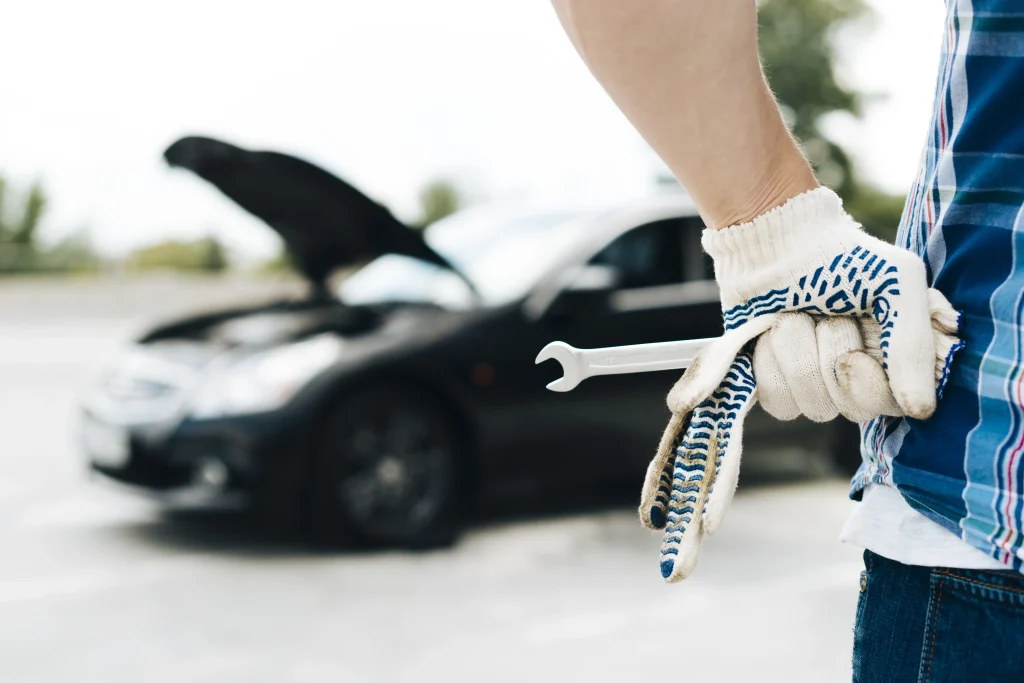 Mobilny serwis samochodowy Wrocław - mechanik w rękawicach z kluczem francuskim, auto z otwartą maską, symbol awarii i naprawy w trasie